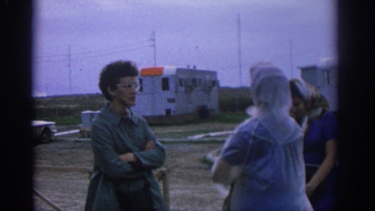 1963 Zurich home-movie frame showing women conversing in an open lot near mobile trailers and utility poles.