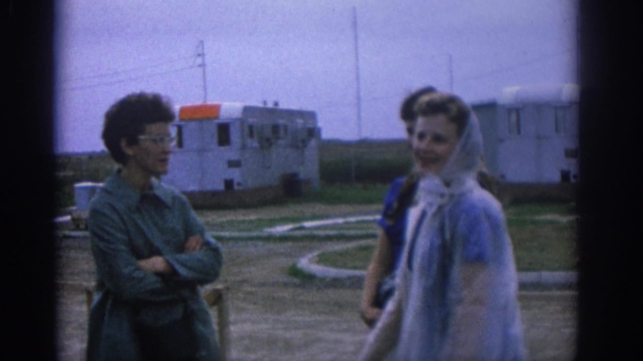 1963 Zurich frame with women in head coverings and a woman in glasses sharing a casual outdoor exchange near trailers.