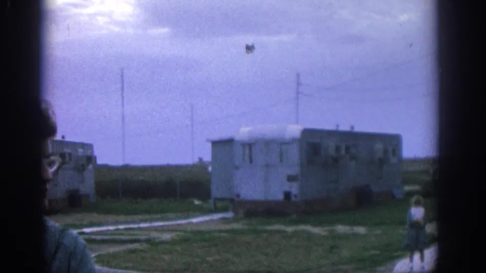 1963 Zurich home-movie view widens to trailers, grass, pale paths, and a partial figure at the left edge.