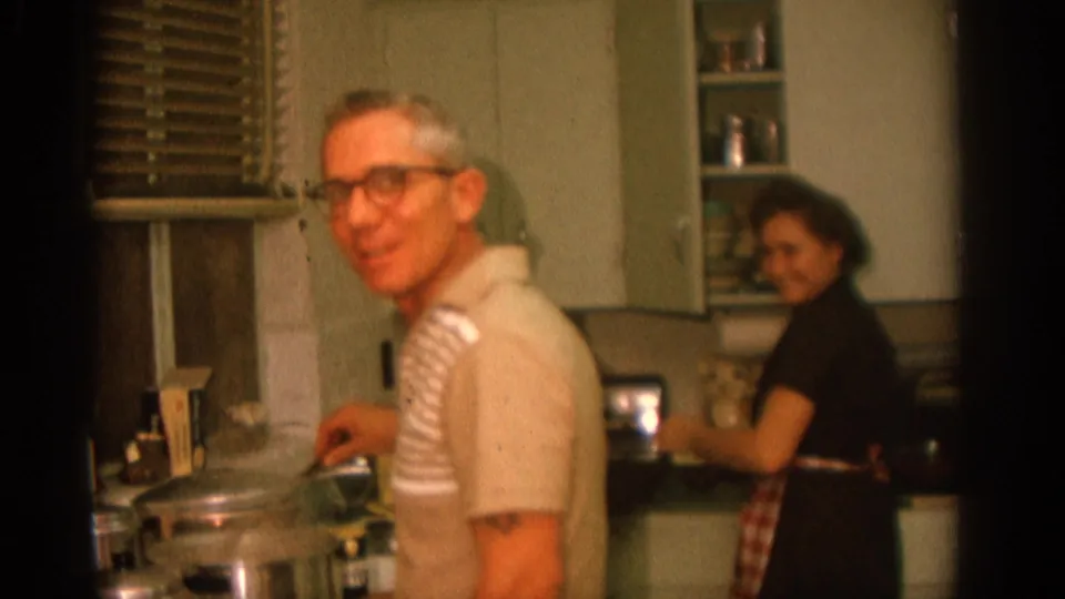 A 1963 Zurich kitchen scene shows the man smiling near a pot while the woman in an apron looks back from the counter.