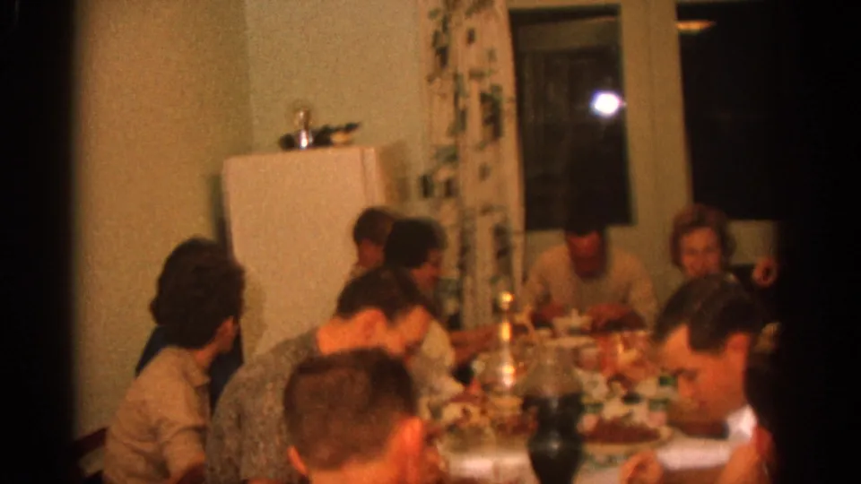 A 1963 Zurich dinner gathering shows several adults seated close together around a table set with food and dishes.