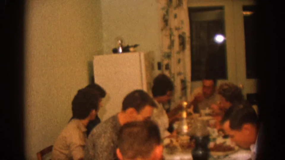 1963 Zurich domestic dinner scene with several adults seated at a crowded table, softly lit by indoor light and candles.