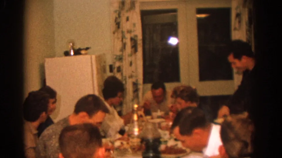 1963 Zurich family dinner frame with seated guests, tableware, candles, and a standing man near the edge of the dining area.