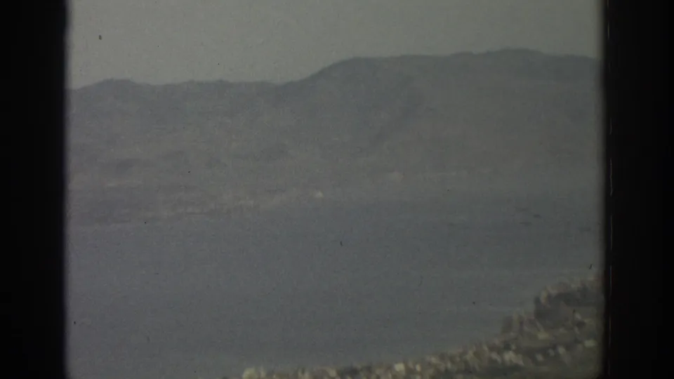 The final frame holds on a broad Swiss lake landscape with mountains and shoreline settlement, softened by haze and dark window framing.