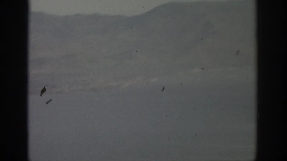 1963 8mm view near Zurich showing hazy mountains and water through an aircraft window frame.