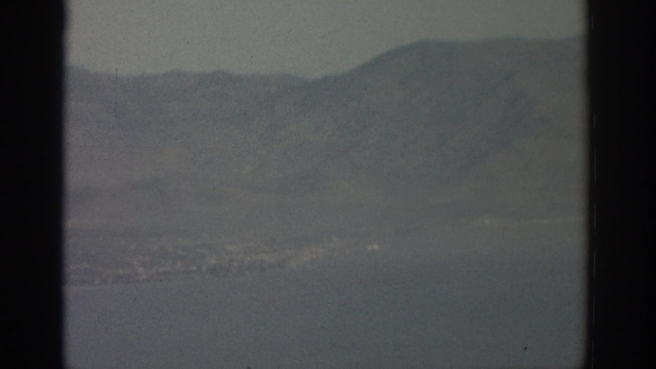 Distant hills, shoreline, and water partly divided by a dark window support.