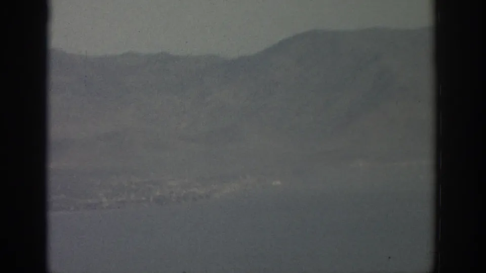 Aerial 8mm frame near Zurich with hills, water, and a faint settlement beyond the aircraft window divider.