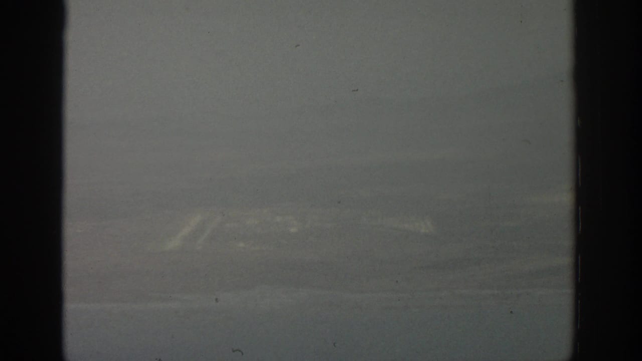 Hazy aerial view through dark airplane window dividers with faint terrain below.