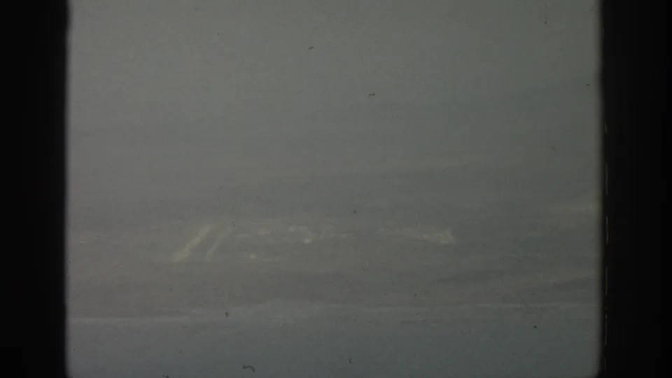 1963 8mm airplane-window view near Zurich, showing a dim, hazy landscape beyond dark vertical window framing.