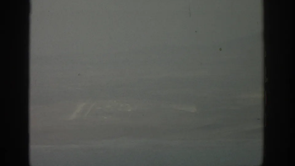 Hazy 1963 8mm aerial view from an airplane window, with indistinct landforms below and dark frame edges.