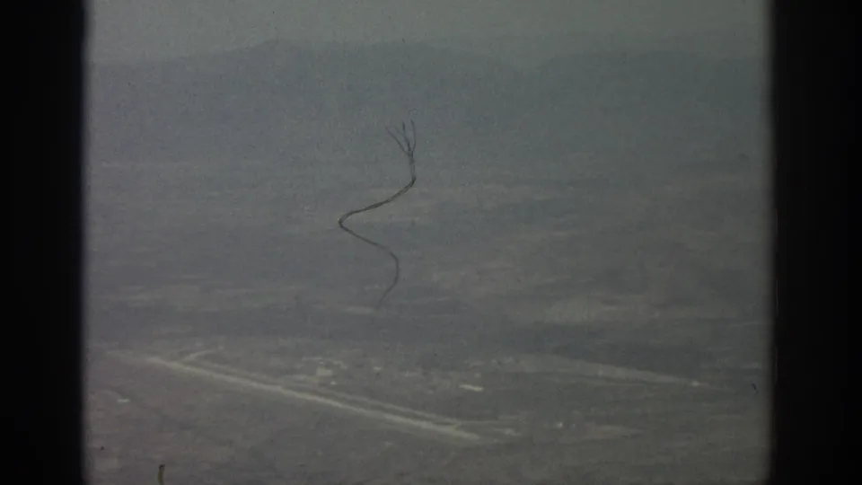 Hazy 1963 aerial home-movie frame with faint roads, scattered light areas, window borders, and visible film scratches.
