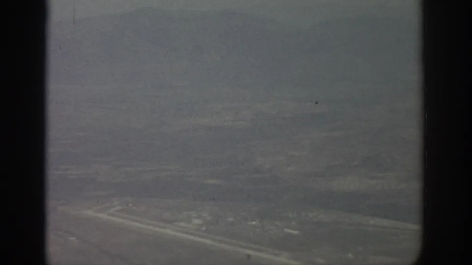 1963 Zurich-area aerial view through a dark airplane window frame, showing hazy open land and distant city texture.