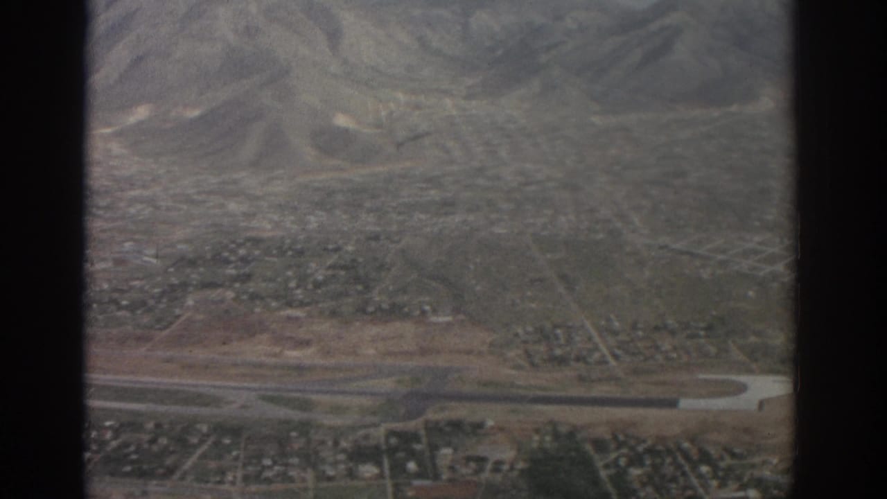 Aerial view over a town edge, fields, roads, and distant mountains.