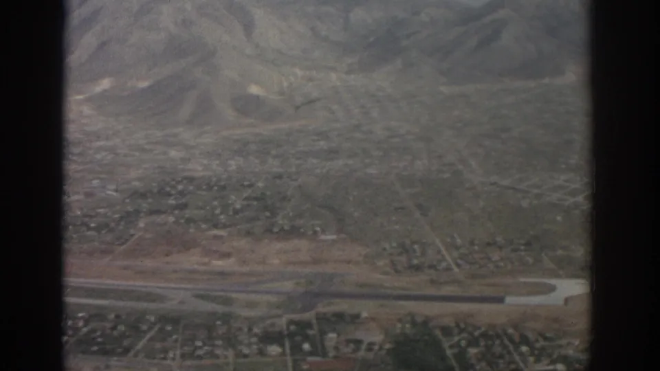 Zurich-area 1963 aerial frame looking over roads, scattered buildings, open land, and mountain terrain beyond.