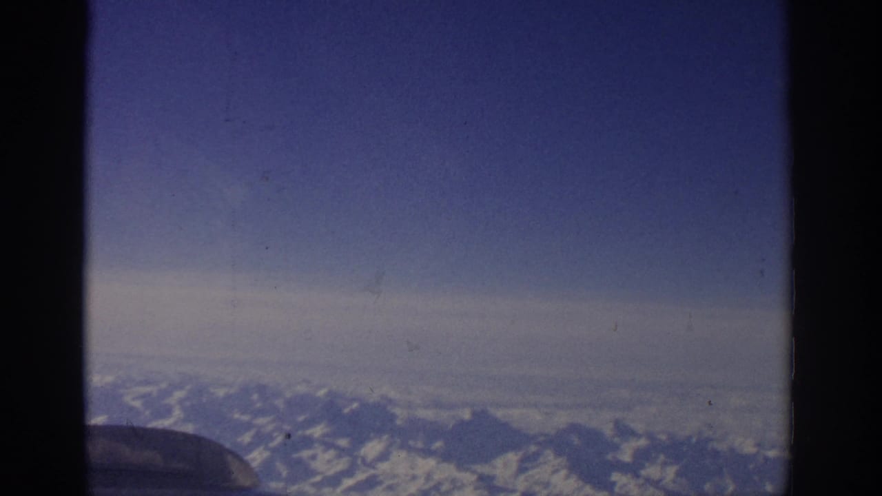 Aerial view of snowy mountain peaks with dark film-frame borders and aircraft detail at lower left.