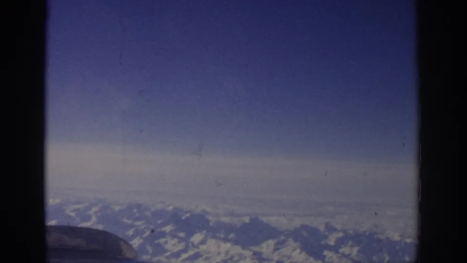 Aerial 8mm frame from a 1963 Switzerland flight, with snow-capped mountains beyond a dark airplane-window edge.