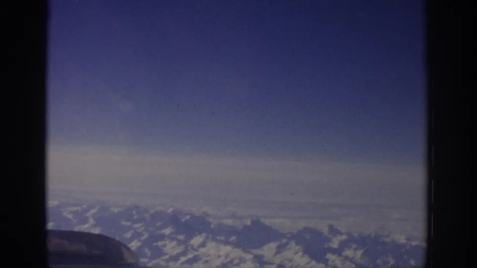 1963 home-movie aerial view over alpine mountains, with the aircraft frame cutting into the foreground.