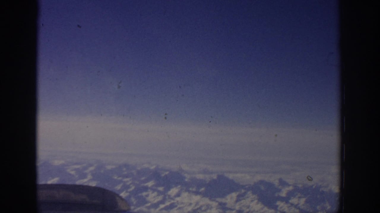 1963 Zurich-linked travel footage showing snow-capped mountains viewed from inside an airplane window.