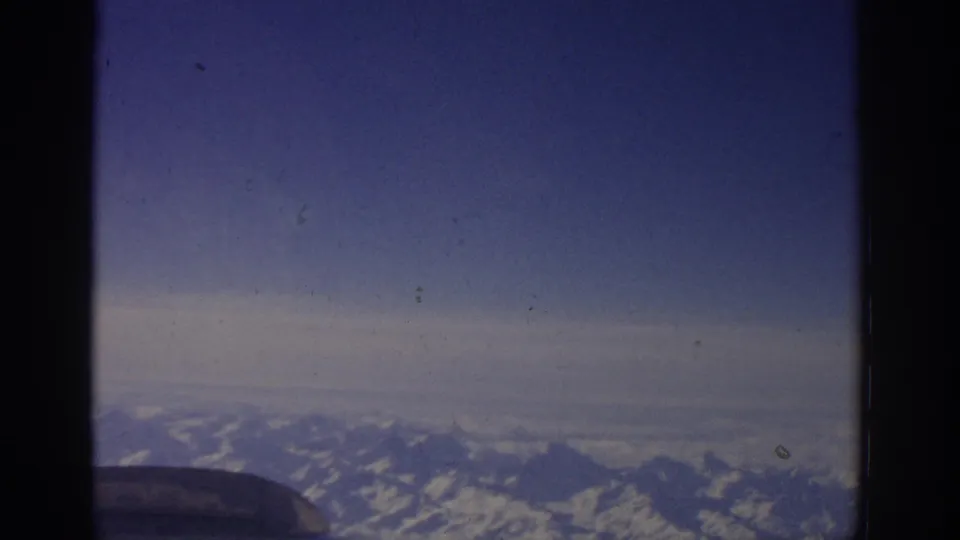 1963 Zurich-linked travel footage showing snow-capped mountains viewed from inside an airplane window.