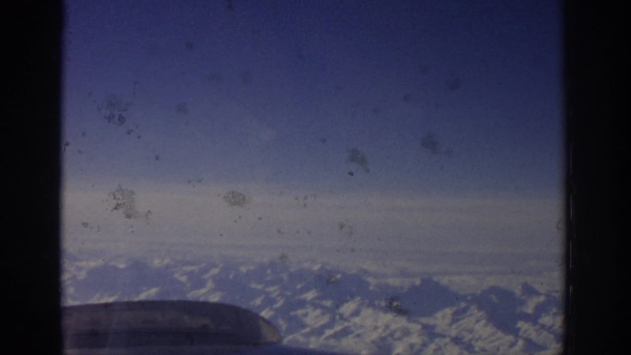 Snow-covered mountains and sky framed by an aircraft window.