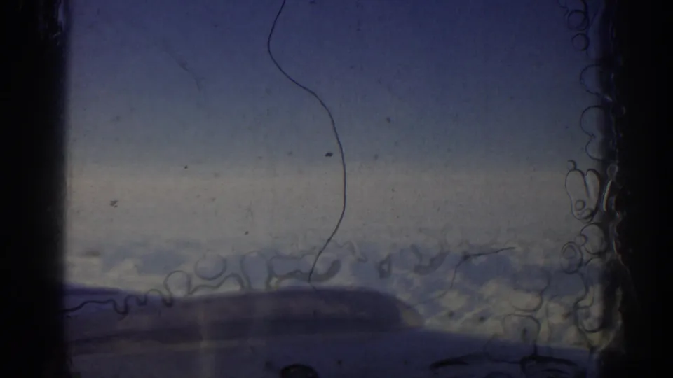Soft 8mm frame of mountains below an airplane window, with strong film dust and edge artifacts.