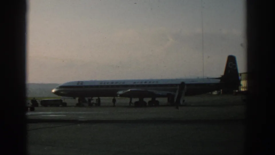 1963 Zurich-linked tarmac view of a commercial airliner with mobile stairs, ground vehicles, and people nearby.