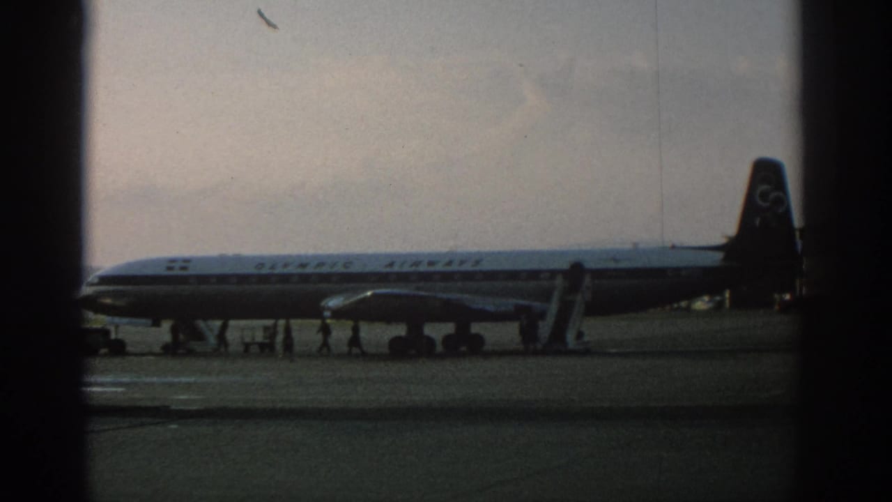 Parked Olympic Airways aircraft with people moving near the stairs on the tarmac.