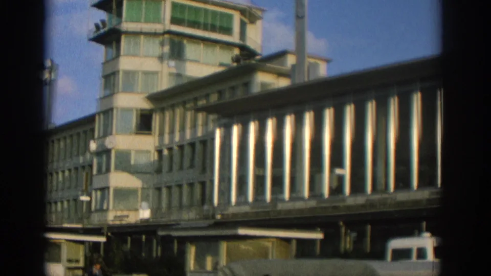 1963 Zurich frame with the building's glass tower and long elevated facade, with a white van partly visible below.