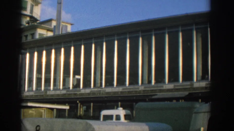 1963 Zurich frame focusing on the long modernist elevated facade, with a white van and larger vehicle partly visible below.
