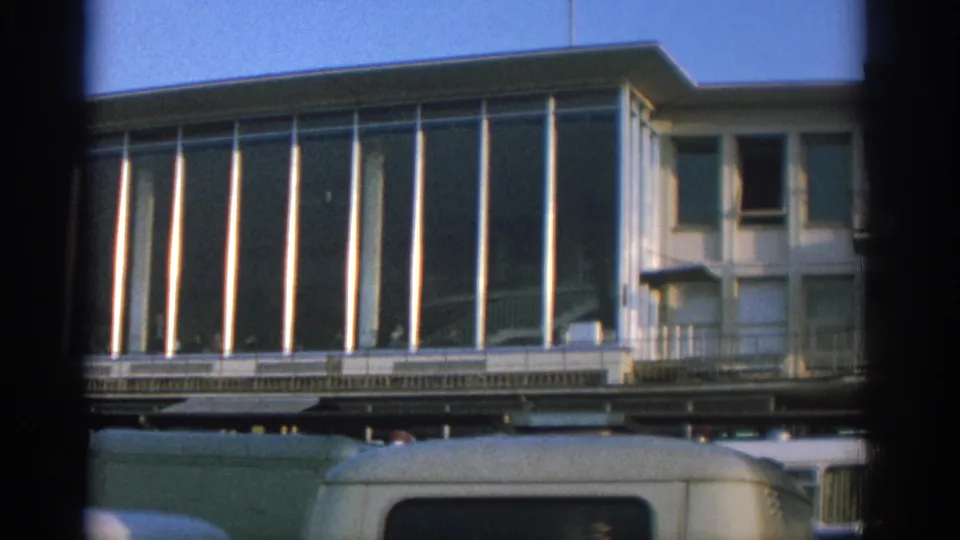 Zurich 1963 frame showing the edge of a modernist facade, adjacent building, and parked vehicles below.
