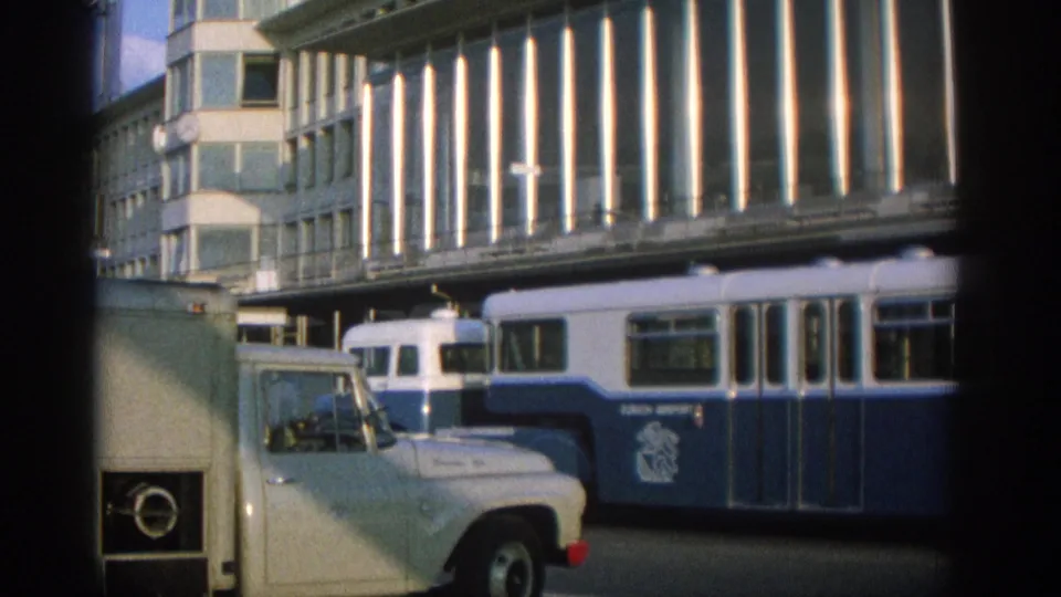 Zurich 1963 street scene with a blue-and-white public bus, parked vans, and a modernist facade overhead.