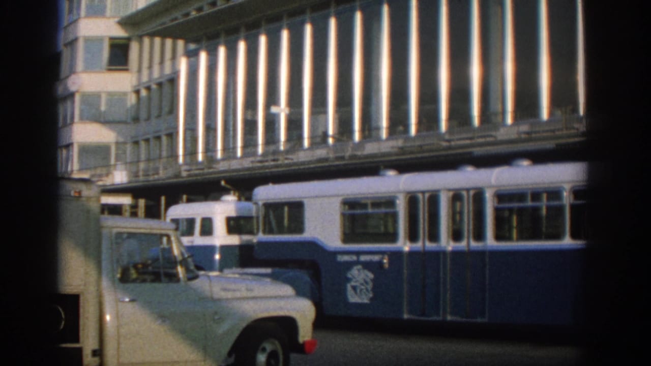 Blue-and-white trolleybus beside a pale utility vehicle on a city street.