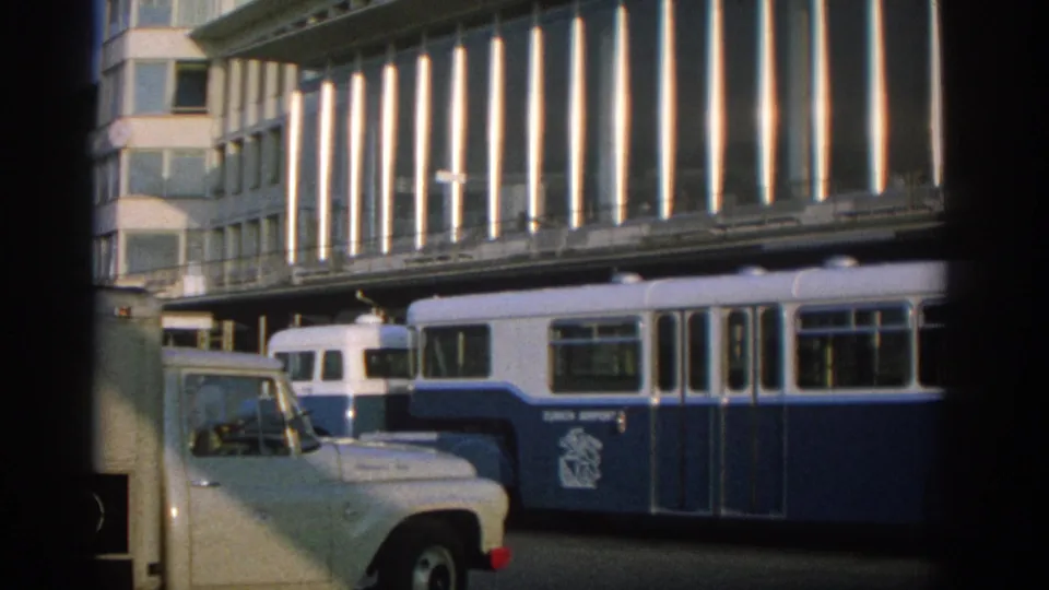 1963 Zurich street view with a blue-and-white public transit vehicle passing beneath a modernist building facade.