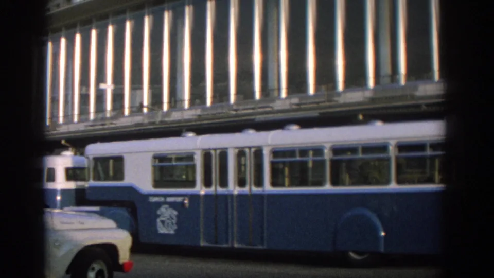 Blue-and-white public transit vehicle in Zurich, seen through dark framing against a modernist street facade.