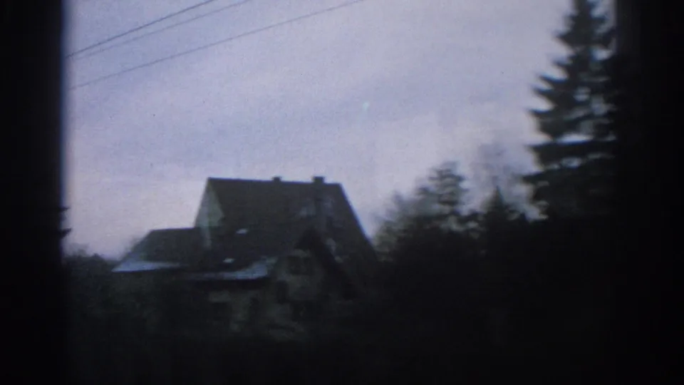 1963 Zurich frame with a small house, dark roofline, trees, and utility wires seen in a moving roadside view.