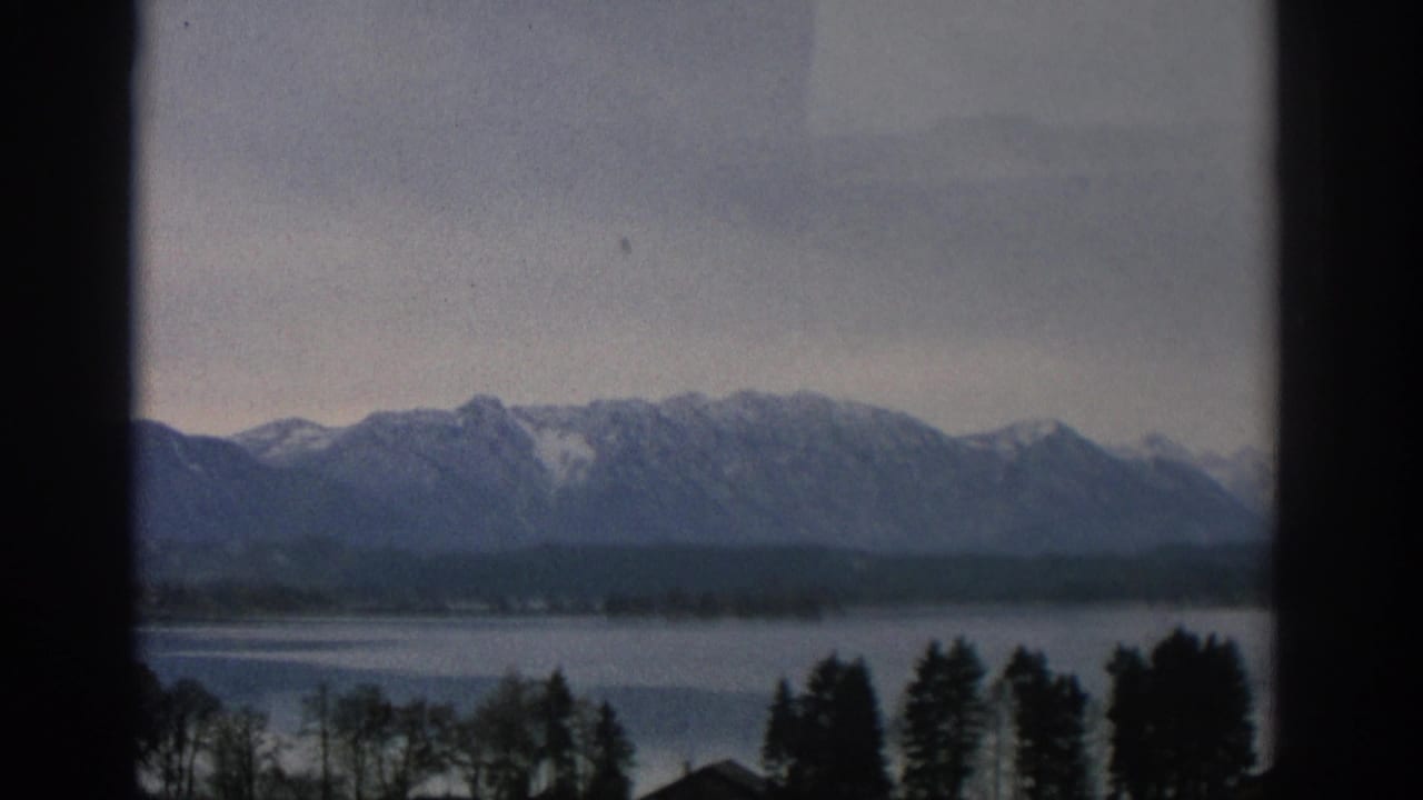 Lake and snow-capped mountains seen through dark window framing.