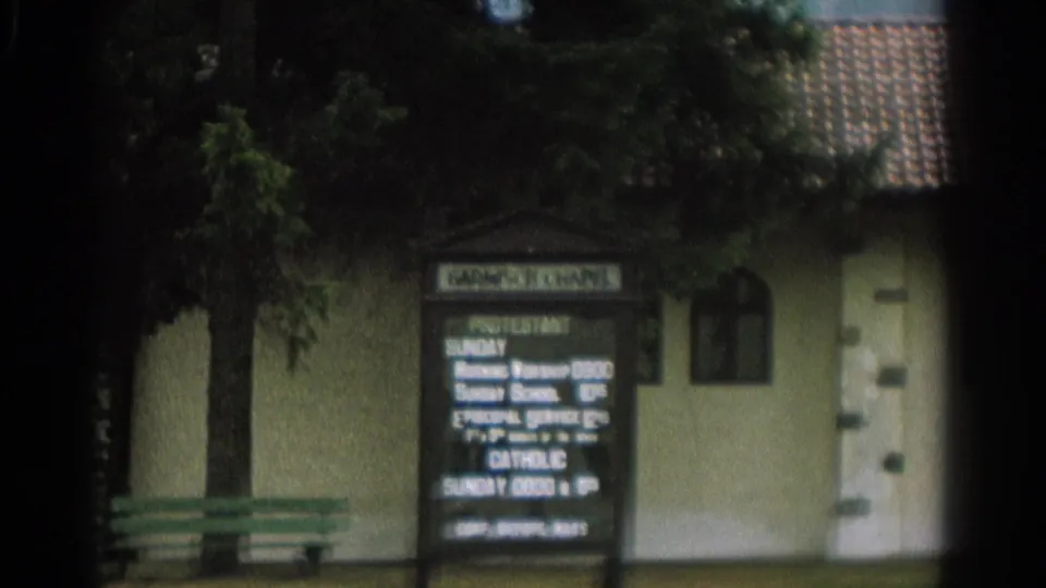 1963 Zurich frame with a freestanding sign listing Protestant and Catholic services before a small chapel with arched windows and a tiled roof.
