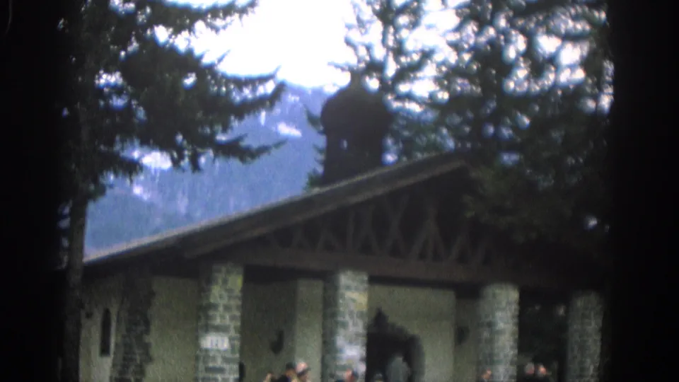 1963 Zurich home-movie frame showing the building facade with stone columns, an arched entrance, trees, and people partly visible below.