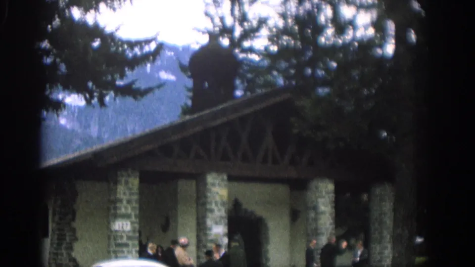 Wedding guests in formal clothing gather outside a stone pavilion in Zurich, Switzerland, with a white classic car nearby.