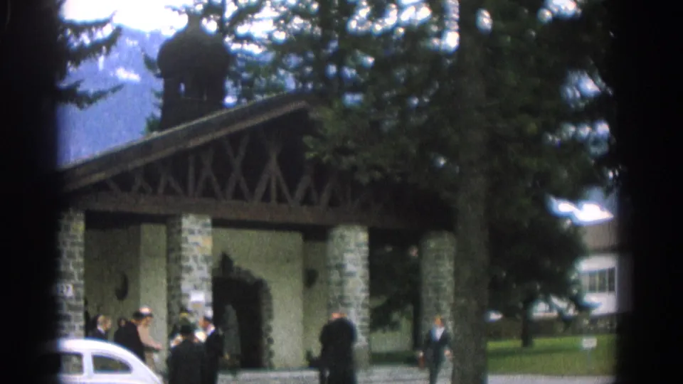 1963 wedding guests appear outside the stone pavilion entrance, with a white car parked close to the doorway.