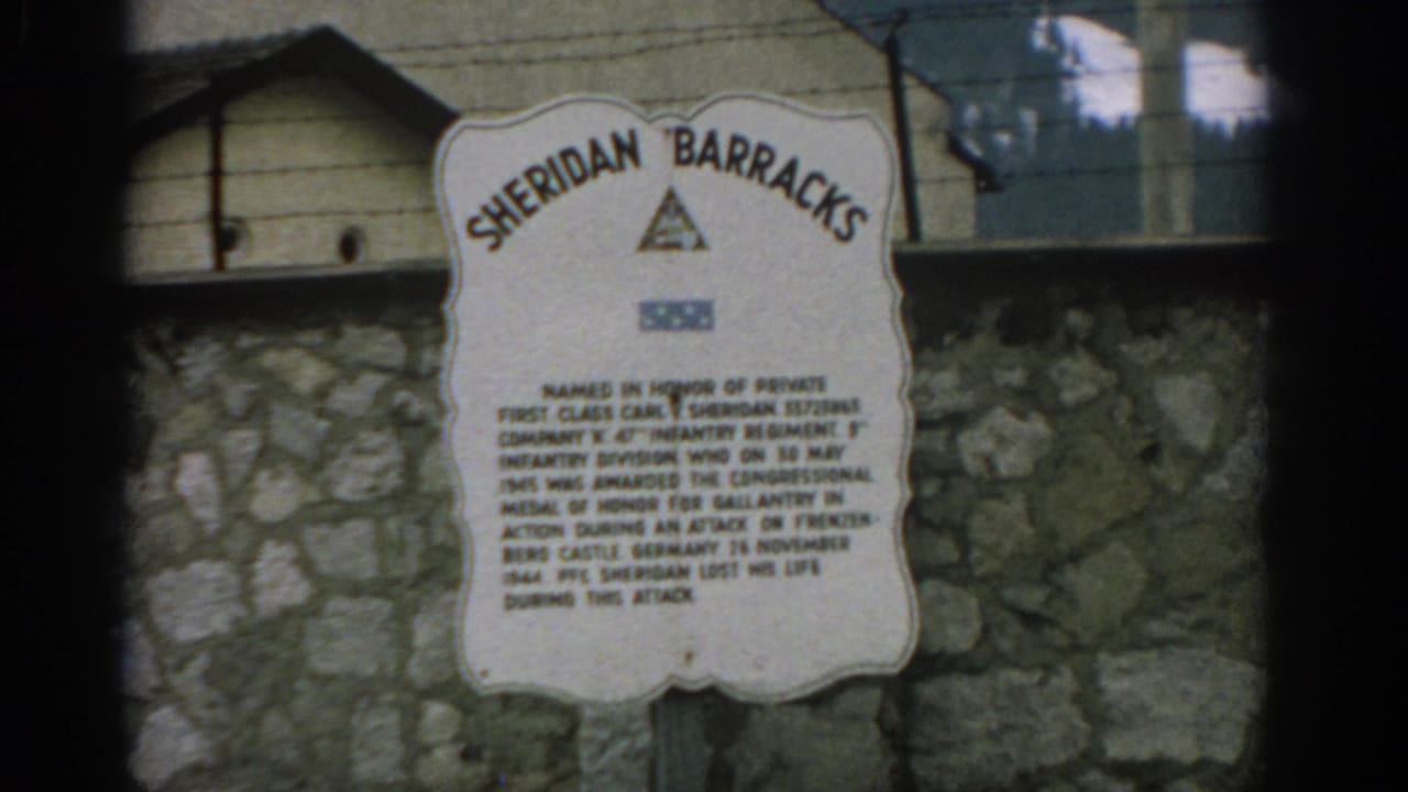 Sheridan Barracks memorial sign mounted on a stone wall below a wooden building.