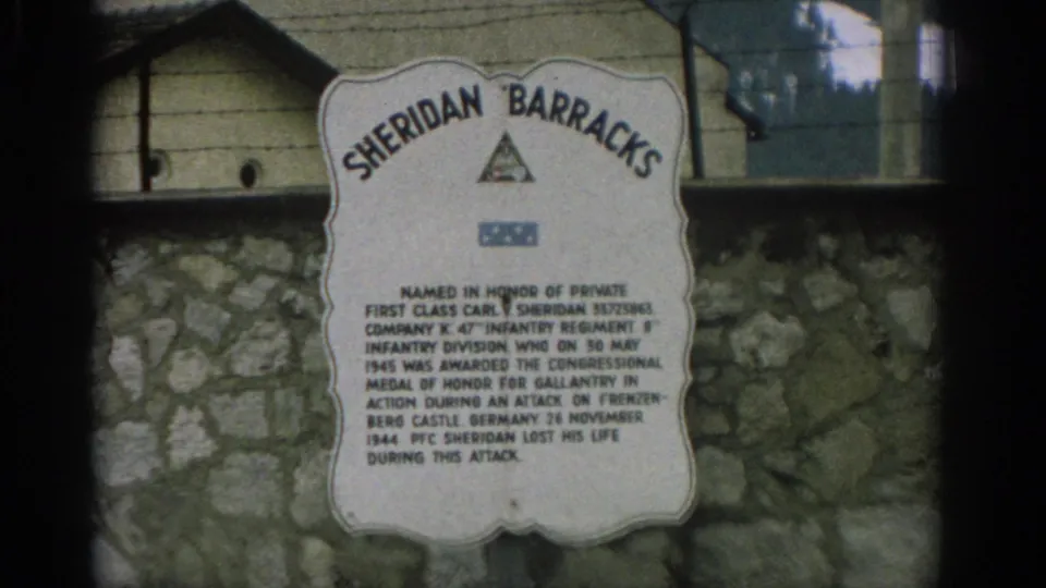1963 Zurich 8mm frame of the Sheridan Barracks memorial sign, with muted color, grain, and slight handheld framing.