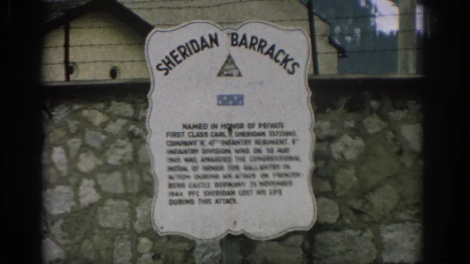 Final 1963 Zurich frame holds on the Sheridan Barracks memorial sign with visible inscription, stone wall, and barracks-like structure.