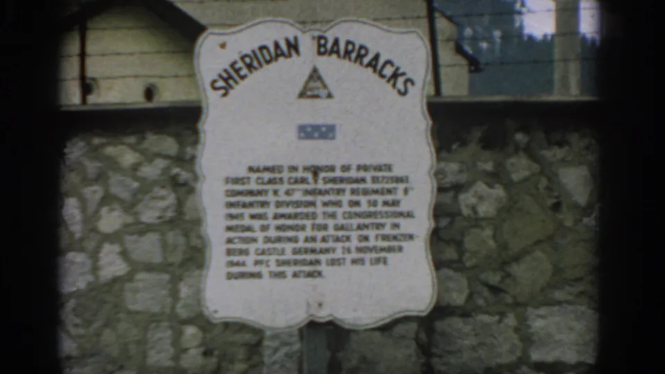 Close 8mm view of the Sheridan Barracks memorial plaque in Switzerland, with the sign text and military symbols visible but soft.