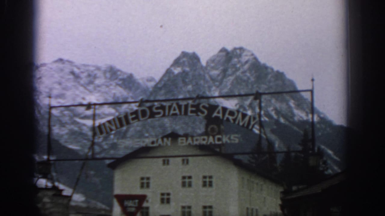 Sheridan Barracks entrance sign and alpine peaks behind a white building.