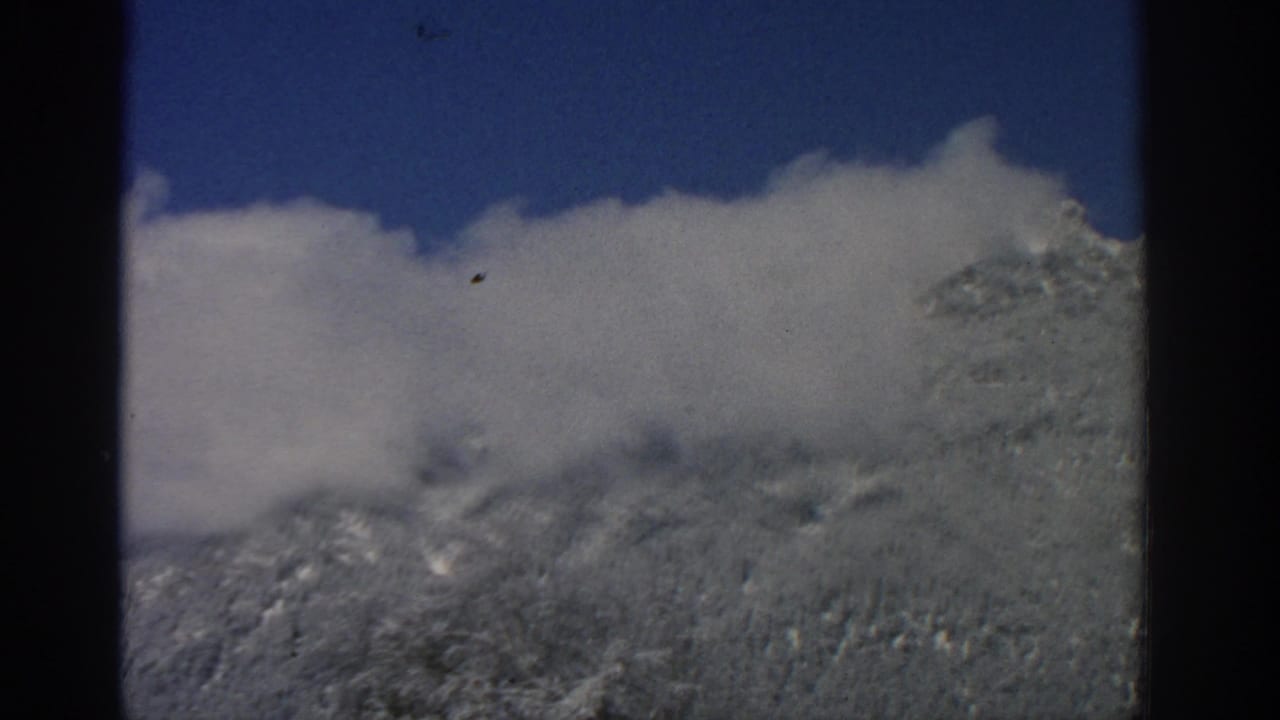 Clouds pass across snowy mountain ridges under a clear blue sky.