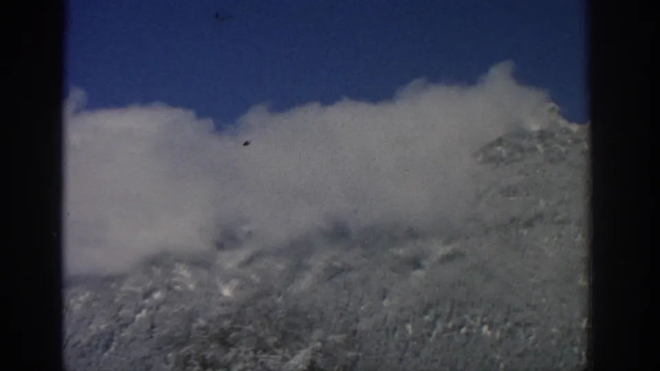 1963 8mm mountain view near Zurich showing snow-bright ridges partly obscured by low white cloud.