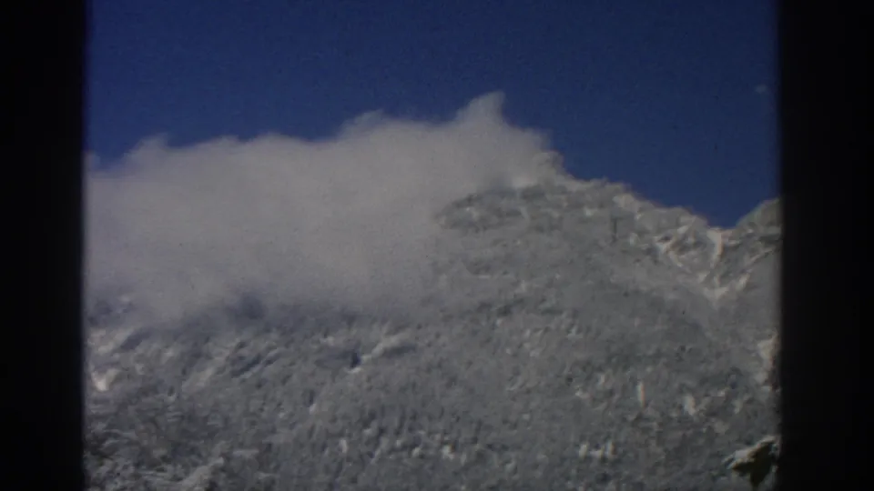 1963 8mm alpine landscape near Zurich with a cloud bank cutting across snow-covered peaks and slopes.