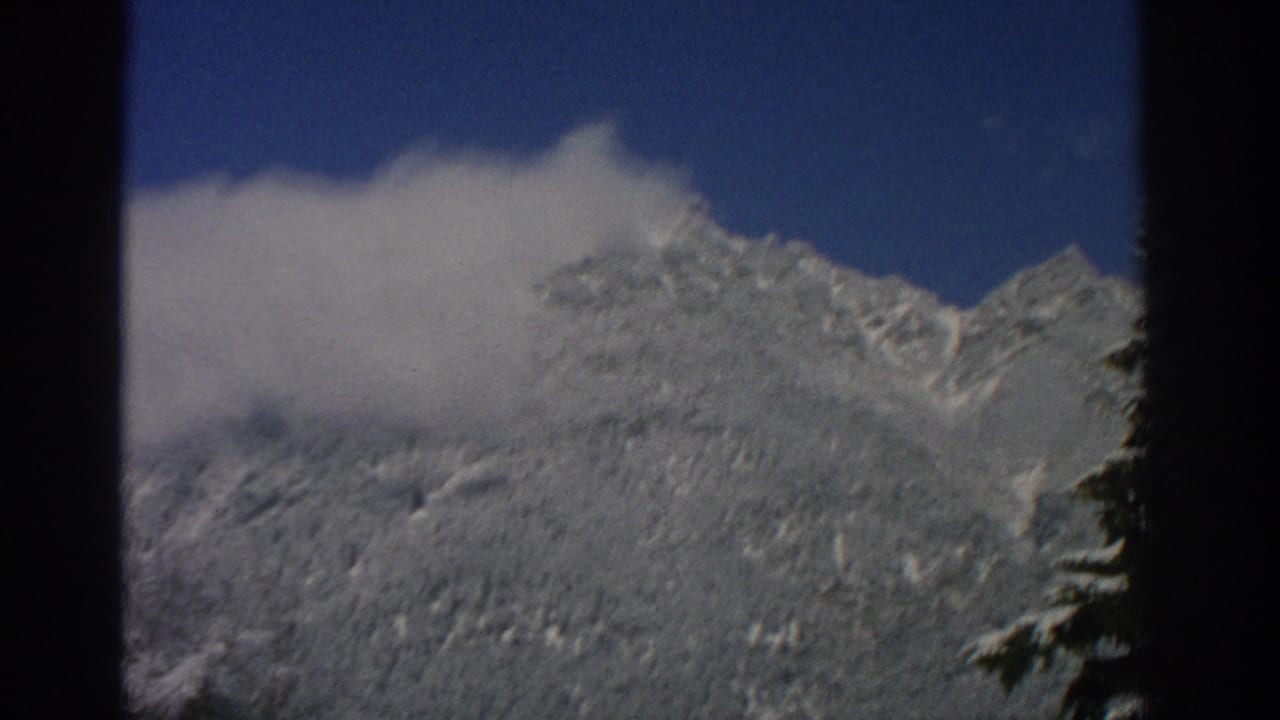 Snow-covered mountain ridge under blue sky with a low white cloud.