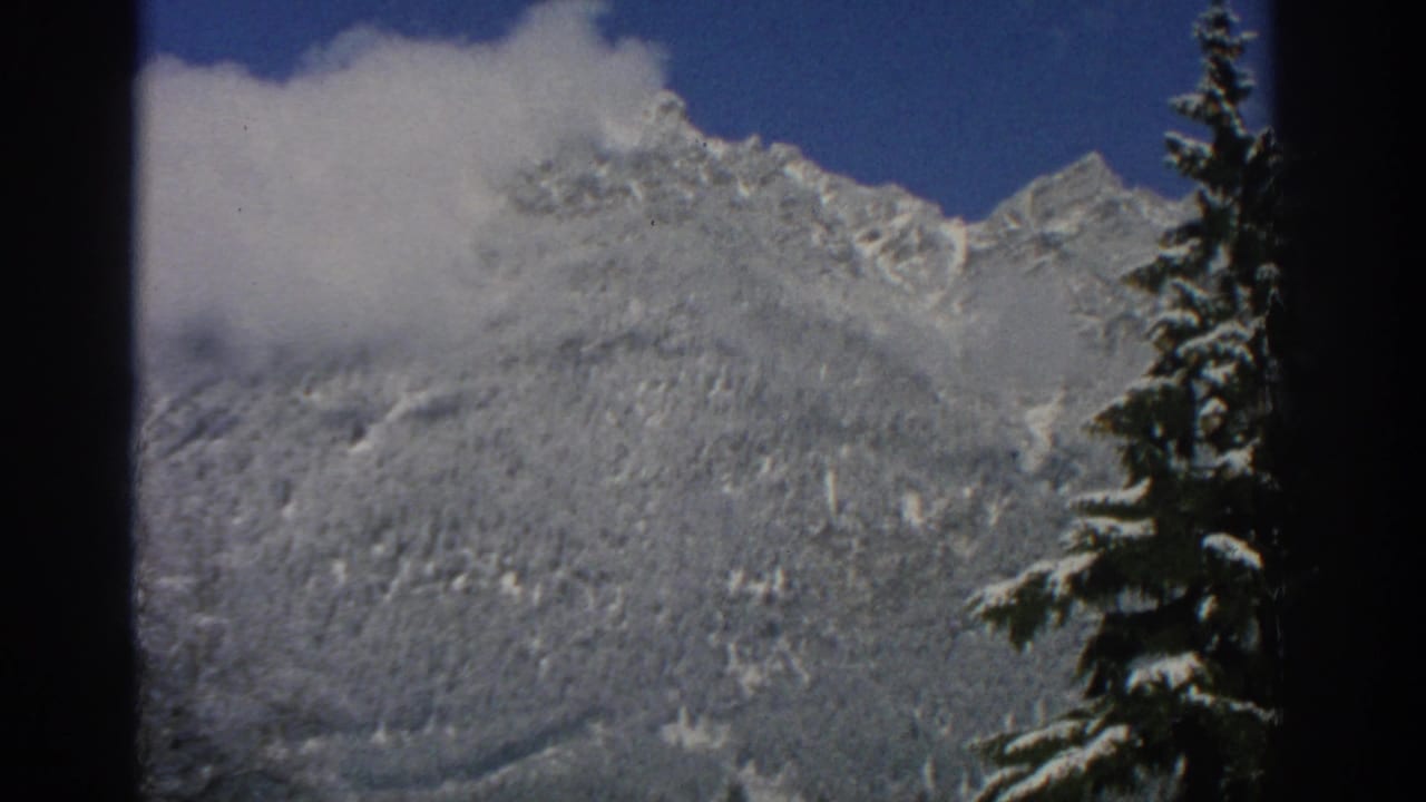 Snowy mountain ridge with a cloud bank and evergreen tree at right.